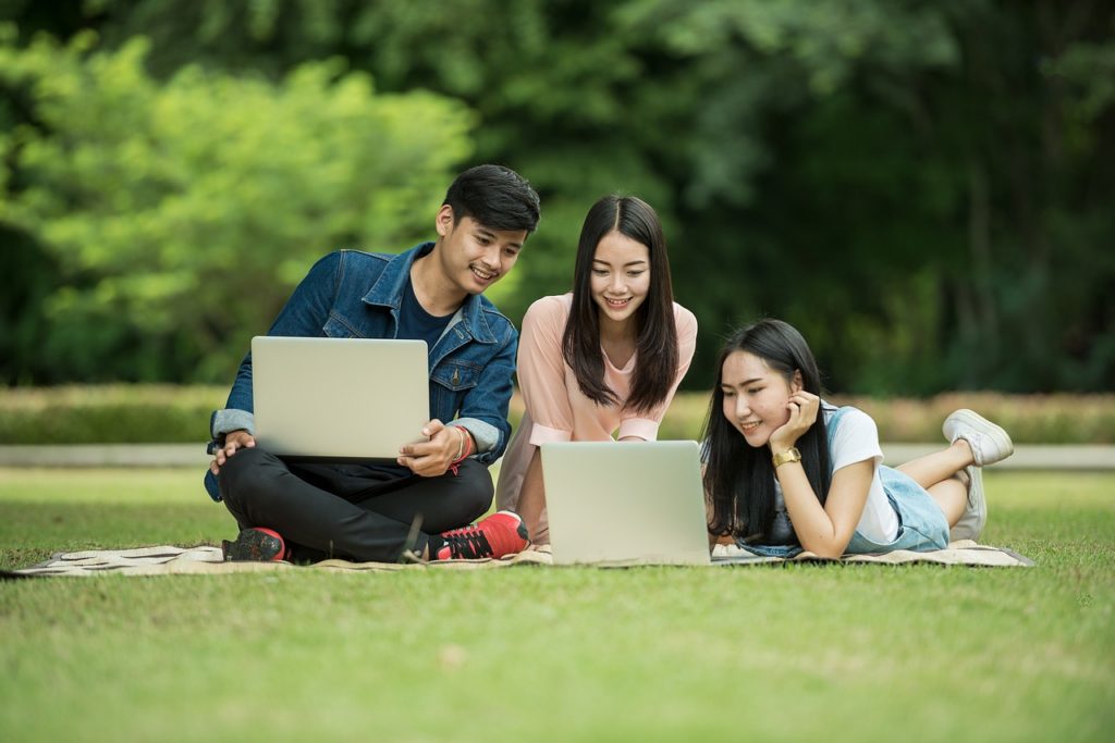 Three students using laptops in a park